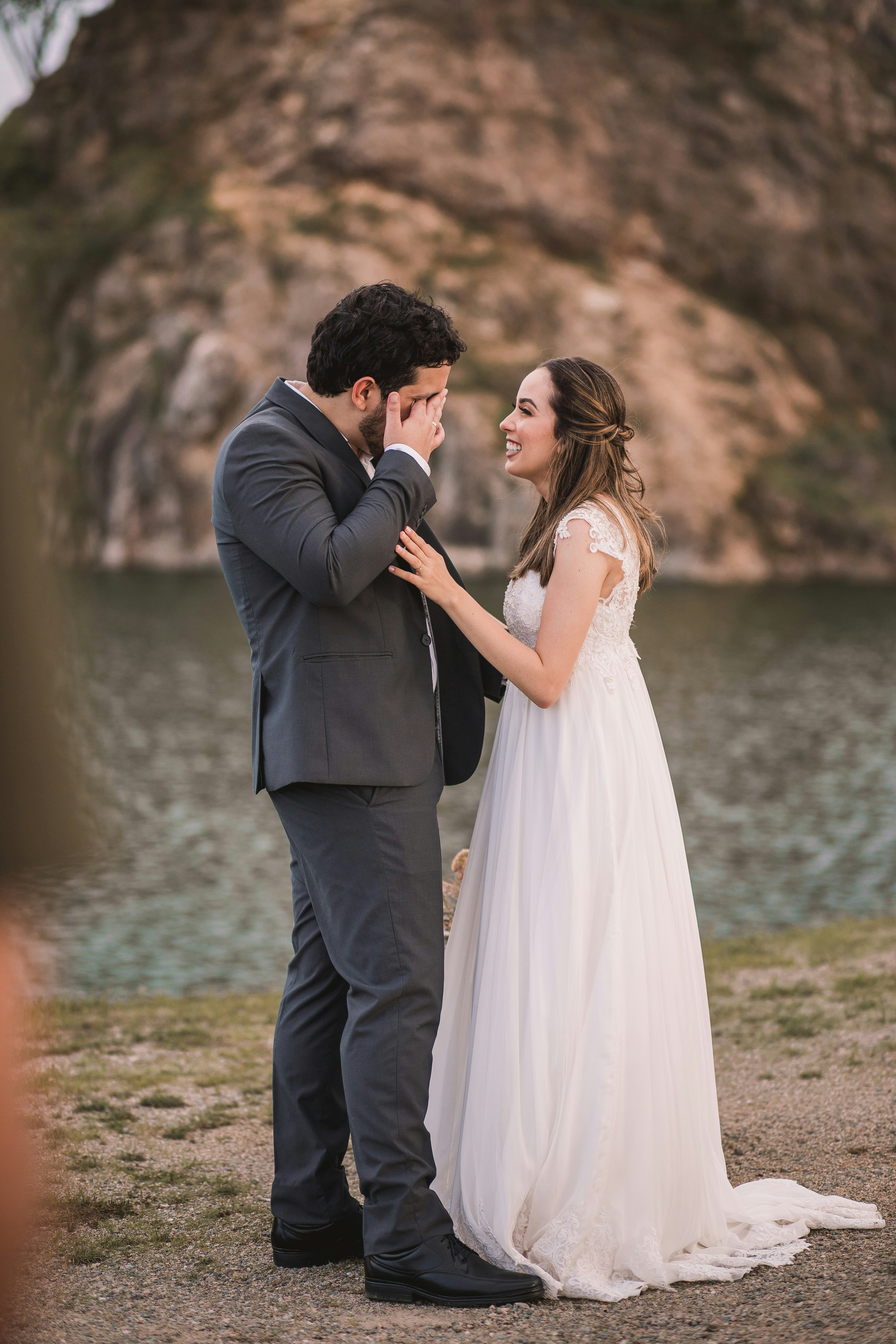 man in black suit kissing woman in white wedding dress on seashore during daytime